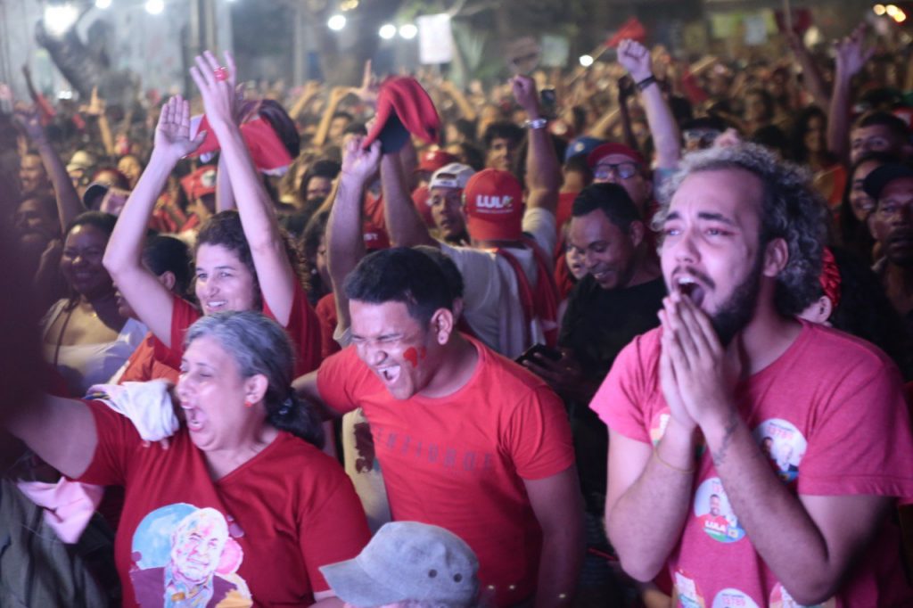 Foto com um grupo de militantes de Lula comemorando com as mãos para cima o resultado da apuração.