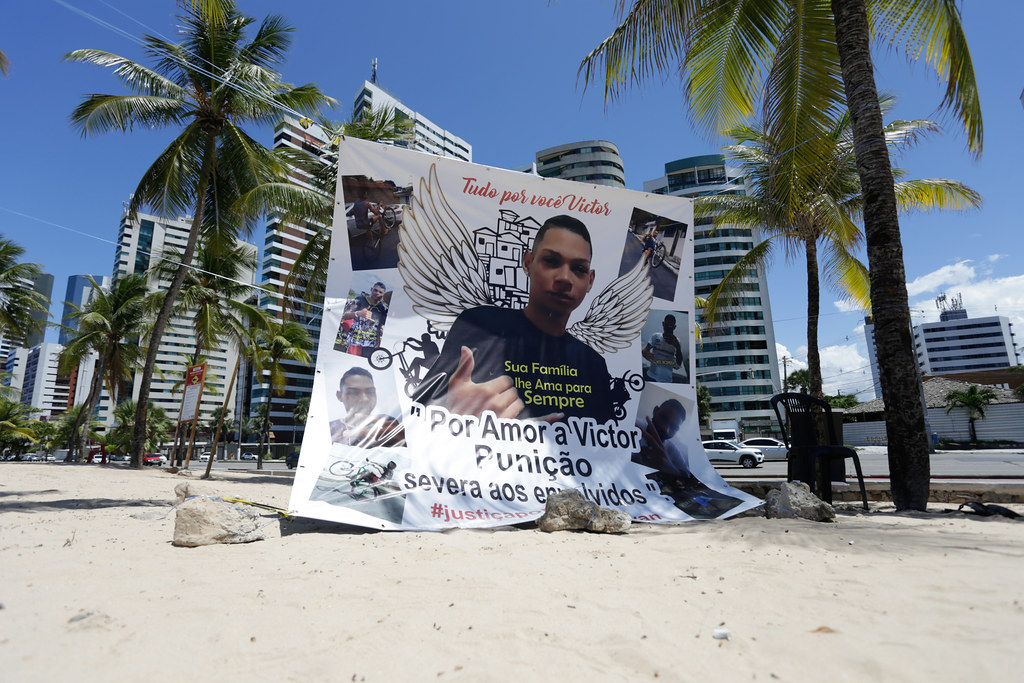 Banner na cor branca com a foto do adolescente negro Victor Kawan, pendurada por cordas entre dois coqueiros na praia de Boa Viagem, em protesto organizado pela família do rapaz.