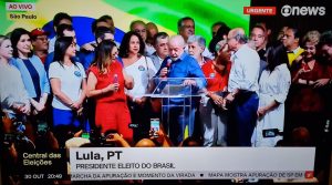 Lula veste camisa azul cercado por vários líderes políticos enquanto discursa após ser eleito presidente