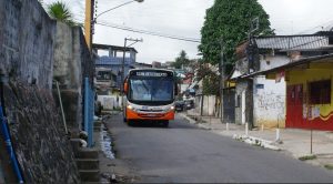 ônibus branco, com pára choque dianteiro laranja, com o letreiro "Nova Descoberta" descendo ladeira na periferia do Recife.
