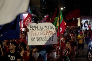 À noite, multidão em passeata com bandeiras vermelhas e do Brasil carrega um cartaz onde se lê Sem anistia para golpistas de Brasília!