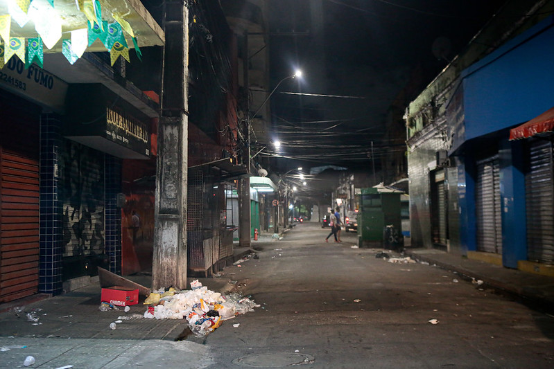 rua estreita escura à noite, com prédios baixos e montes de lixo.