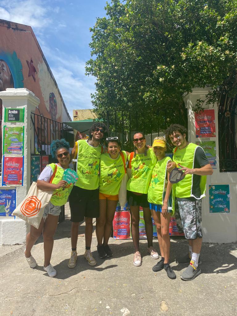 Grupo de seis pessoas, homens e mulheres de diferentes etnias, usam camisetas verde neon da equipe da Escola Livre de Redução de Danos, posando em frente à portão de casa no sítio histórico de Olinda.