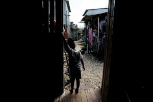 Imagem de uma menina pequena, na contraluz, à porta de um barraco de madeira numa favela