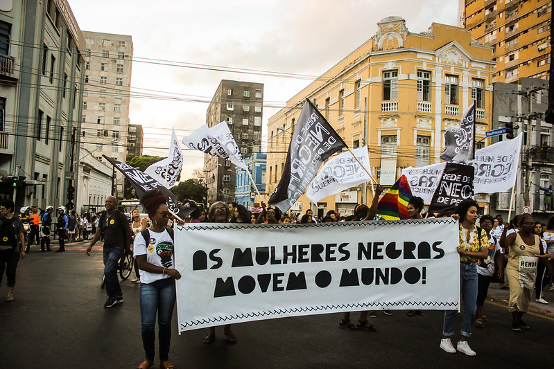 Grupo de mulheres durante passeata carregam faixa branca com as letras pretas com a inscrição As mulheres negras movem o mundo