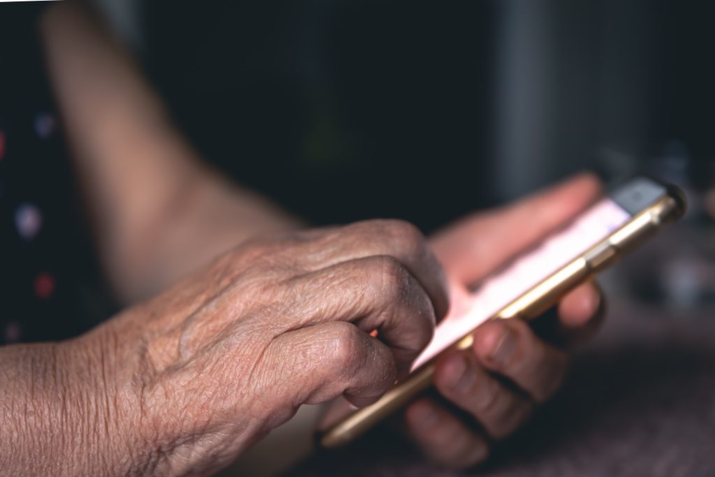 Mãos de uma pessoa idosa negra segurando um telefone celular em close 