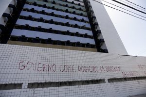 Fachada de prédio abandonado em Maceió pichada com a frase Governo come dinheiro da Braskem.