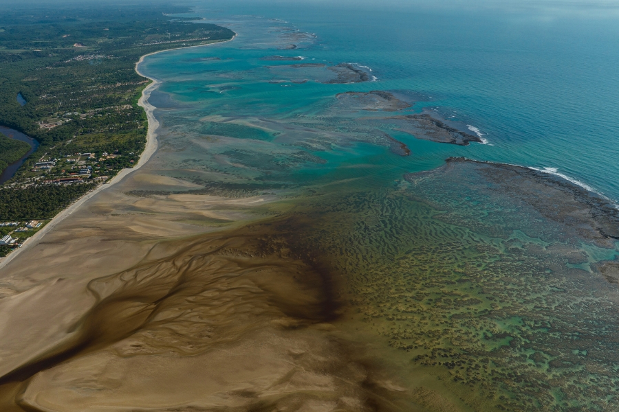 Foto colorida de vista aérea de uma praia deserta com arrecifes, bancos de areia e águas azuis cristalinas