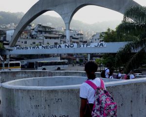Menina negra com uniforme escolar e mochila rosa nas costas observa faixa com a frase "ministra negra no STF já" colocada nos arcos da praça da apoteose do sambódromo, no Rio de Janeiro.