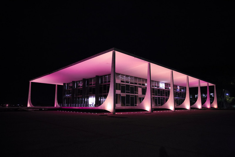 Foto noturna da fachada do STF iluminada com luzes cor de rosa.