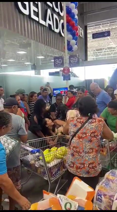 No centro da foto, uma mulher caída em meio a uma multidão, empurrando carrinhos de supermercado.