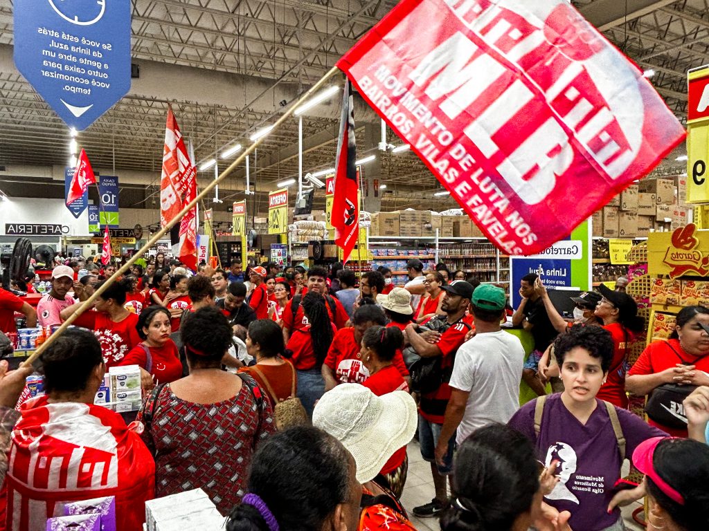Manifestantes com bandeiras e camisas vermelhas lotam corredores de supermercado.