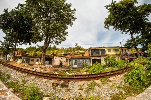 foto colorida do bairro de Flexais, com linha de trem em primeiro planoe fileira de pequenas casas logo após a estrada de ferro, com uma grande árvore de cada lado da imagem.
