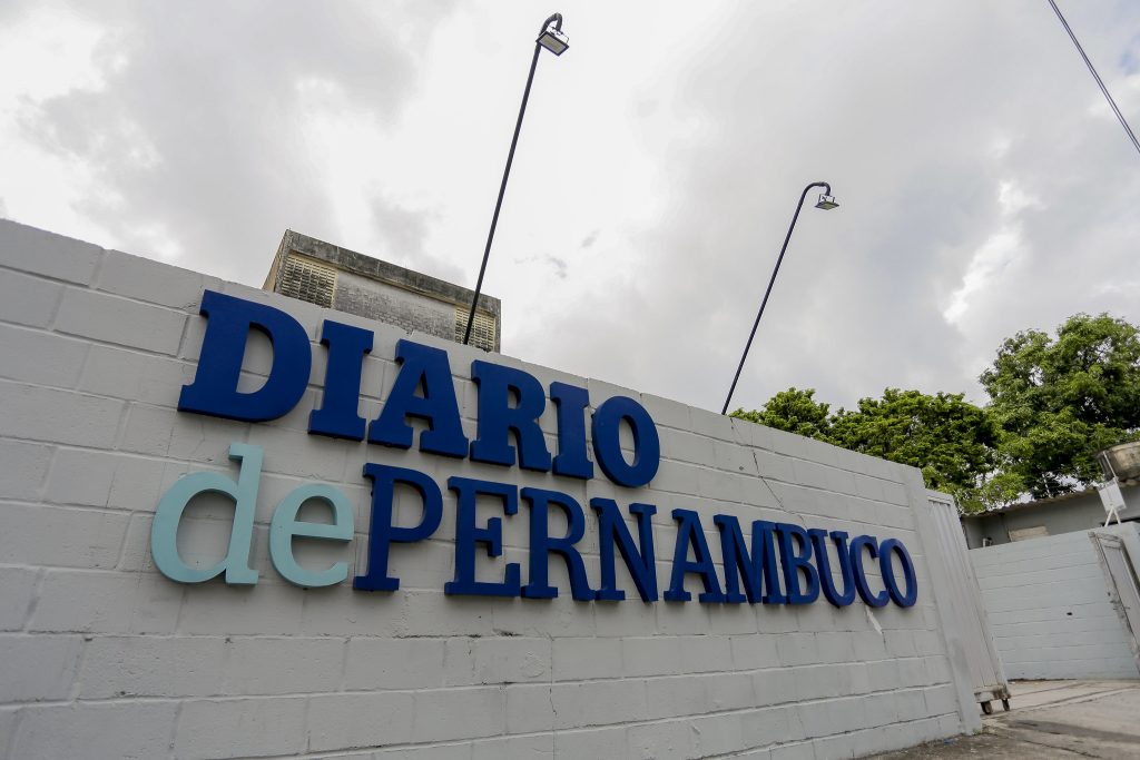 Fachada da sede do jornal Diário de Pernambuco, cujo letreiro aparece em letras azuis em painel de tijolos de cimento branco.