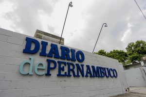 Fachada da sede do jornal Diário de Pernambuco, cujo letreiro aparece em letras azuis em painel de tijolos de cimento branco.
