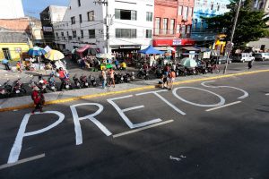 Foto feita a partir de um ponto mais elevado da palavra pretos pintada com tinta branca no asfalto de uma avenida no centro do Recife