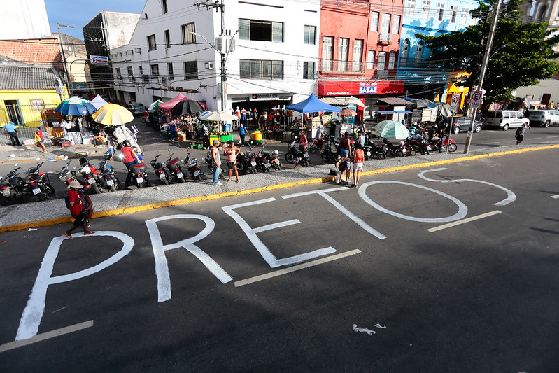 Foto feita a partir de um ponto mais elevado da palavra pretos pintada com tinta branca no asfalto de uma avenida no centro do Recife