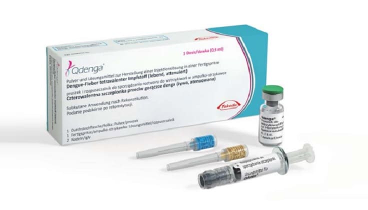 Foto colorida de caixa da vacina Qdenga, com ampolas e seringa do lado de fora da caixa.