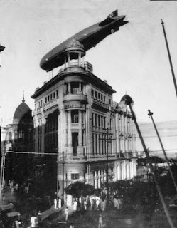 Foto antiga em preto e branco de uma edifício do bairro do Recife com um zeppelin sobrevoando, dando a impressão de que o dirigível faz parte da estrutura do prédio em estilo clássico.