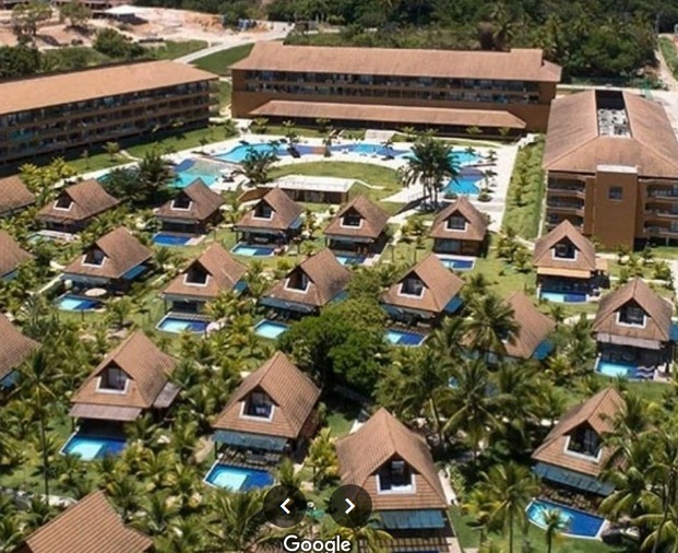 Foto aérea do Ecoresort Praia dos Carneiros, empreendimento luxuoso com bangalôs com piscinas individuais e muitos coqueiros, tendo ao fundo uma piscina maior em formato de ferradura e construções baixas.