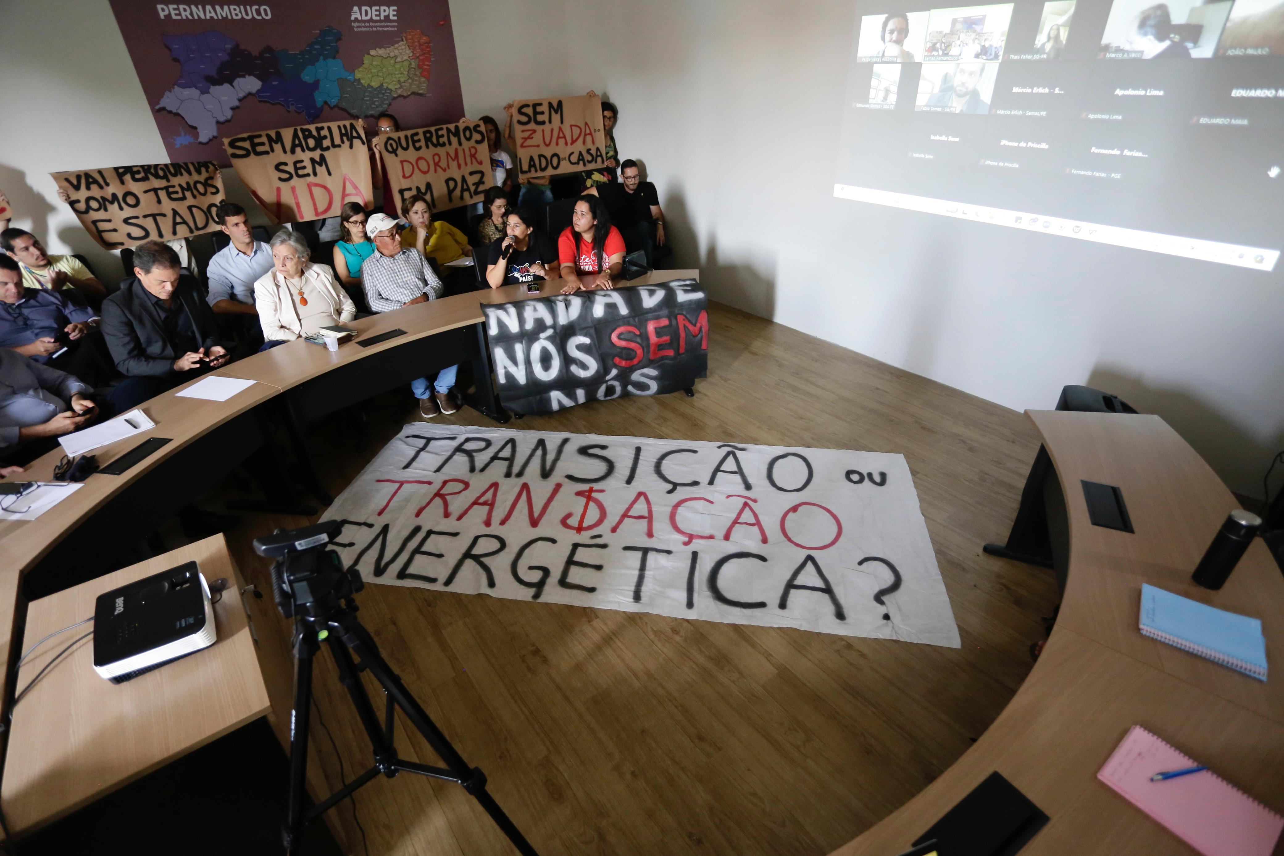 Foto da reunião do GT das renováveis, mostrando a sala cheia com uma faixa em destaque escrita transição ou transação energética?.