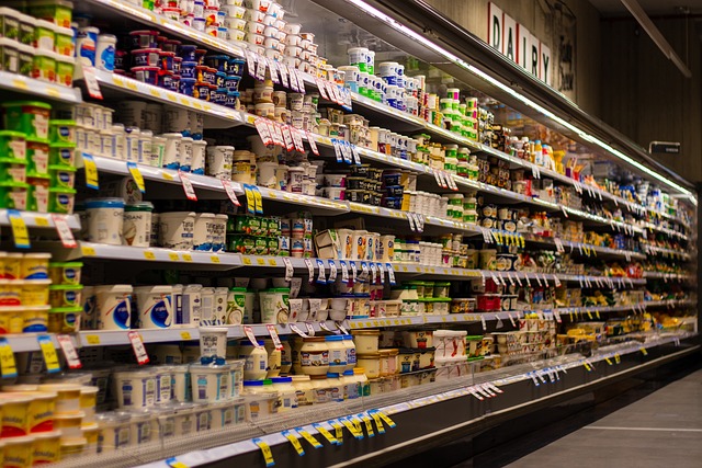 Esta imagem mostra uma prateleira de supermercado com variedade de produtos organizados em prateleiras refrigeradas em um supermercado. As prateleiras estão repletas de itens como leite, iogurte, queijo e outros produtos relacionados, cada um em embalagens coloridas e distintas.