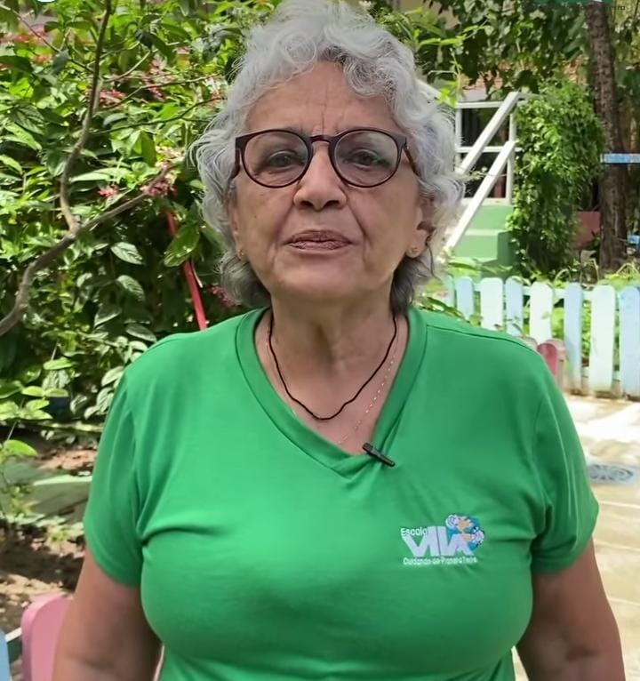 Foto de Fátima Limaverde, mulher branca, idosa, de cabelos brancos, usando óculos de aro preto e camiseta verde. Ela foi fotografada em um ambiente que parece ser um quintal.