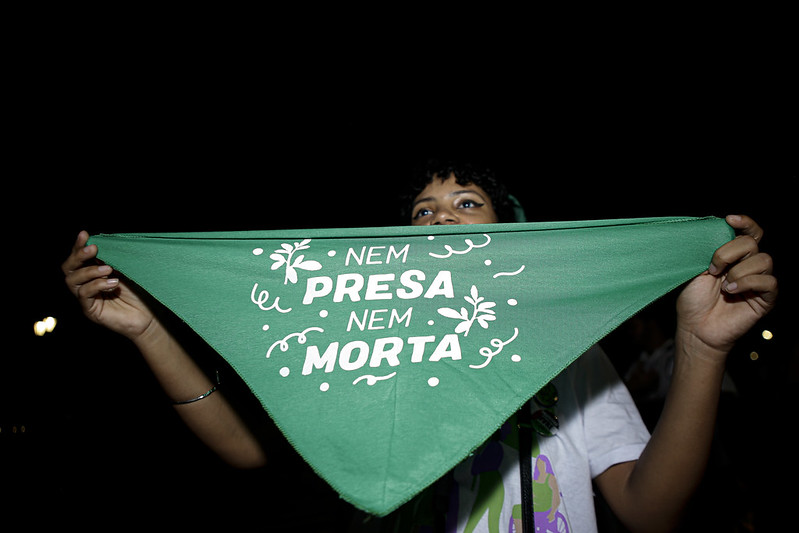 Imagem mostra jovem segurando uma bandeira verde em defesa do direito ao aborto com os dizeres nem presa nem morta