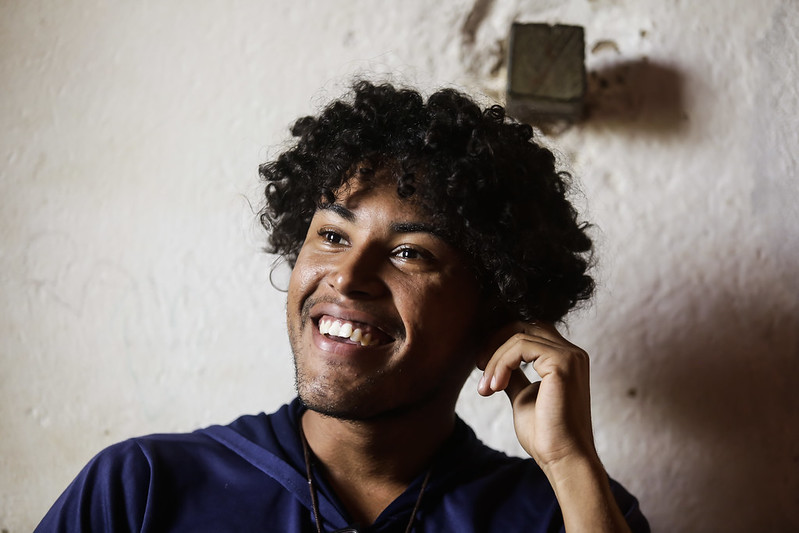 Foto de Jair Cardoso de Matos. Jovem negro, de fartos cabelos encaracolados. Na foto, ele está sorrindo, com a mão esquerda tocando seus cabelos e usando uma camisa ou blusão azul escuro.