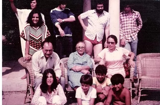 Foto envelhecida de um grupo de 12 pessoas posando para a câmera em um ambiente externo, provavelmente um terraço, com uma coluna no meio e cadeiras de palha onde estão sentadas três pessoas na fileira central, tendo à esquerda Miguel Arraes (homem branco, calvo, curvado), uma idosa de óculos, vestido azul e braços cruzados no centro e uma mulher de vestido branco, óculos escuros à direita. Aos pés dessas três pessoas, estão quatro crianças sentadas no chão. Atrás das pessoas mais velhas que estão sentadas nas cadeiras, há cinco adultos, incluindo uma mulher jovem, de cabelos compridos e vestido estampado. Todas as pessoas estão usando roupas informais.