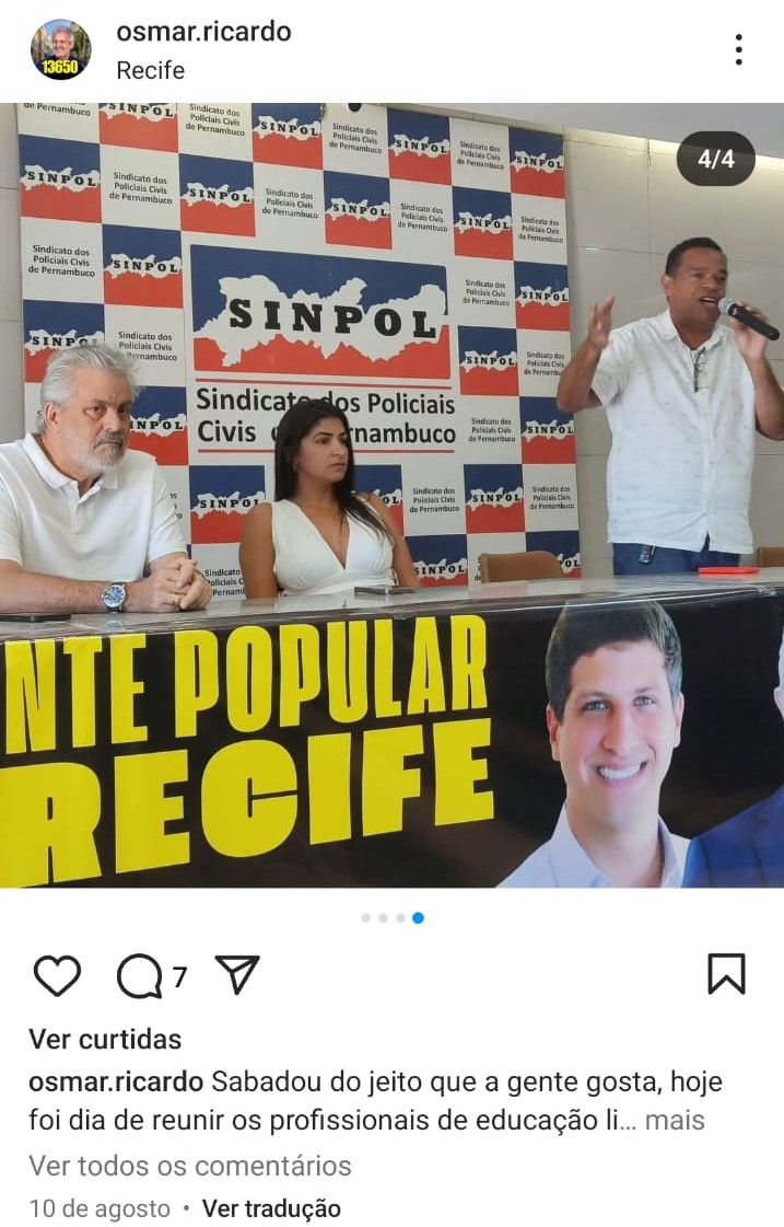 Imagem capturada de uma postagem do perfil do instagram do vereador Osmar Ricardo. Ele está à esquerda da imagem, usando uma camisa pólo branca, sentado atrás de uma mesa com as mãos juntas sobre a mesa. Ele é um homem idoso, de fartos cabelos e barba grisalhos. No centro da mesa há uma mulher jovem, de cabelos pretos lisos, usando um vestido branco. À direita há um homem negro, de meia-dade, de cabelos pretos , falando ao microfone enquanto gesticula bastante.