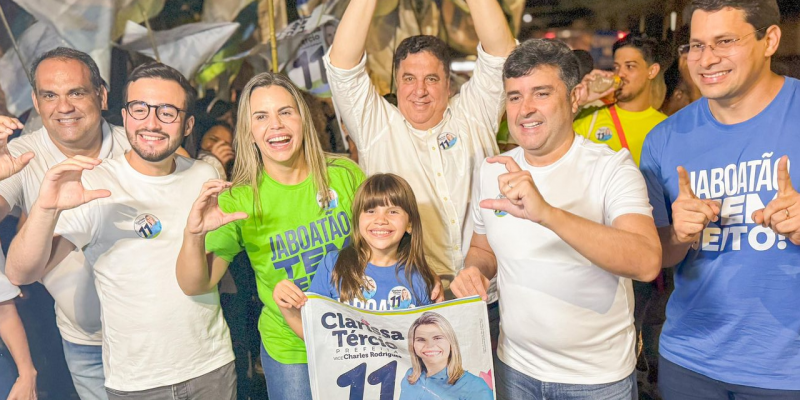 Grupo de sete pessoas formado por cinco homens brancos adultos, uma mulher loira adiulya e uma criança de cabelos castangos, em ato de campanha de Clarissa Tércio. os adultos estão fazendo o sinal de letra c com as mãos.