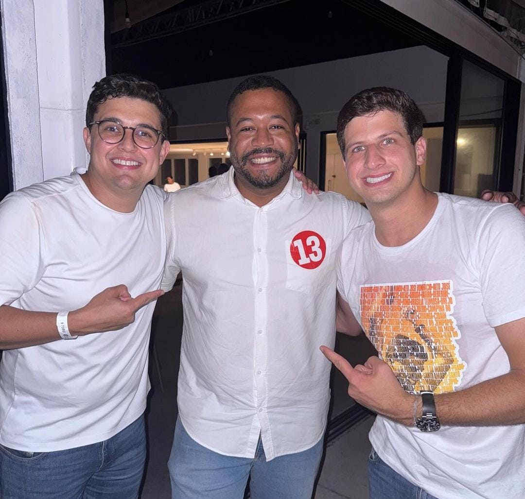 Foto de Victor Marques, Vinicius Castello e João Campos posando para a foto em pose festiva, comemorando vitória nas eleições. Os três são homens jovens, vestidos de branco. Marques (á esquerda) e Campos (à direita) são brancos, enquanto Vinicius,ao centro, é negro e está com um adesivo vermelho com o número 13 no peito.