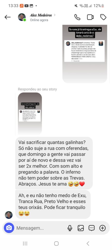 A imagem é uma captura de tela de uma conversa no Instagram. Nela, há uma troca de mensagens entre duas pessoas. A primeira mensagem no topo é uma publicação de story que menciona o nome de uma pessoa e faz referência a Exu, uma entidade da Umbanda e do Candomblé. Abaixo, há uma resposta a essa publicação, em tom provocativo, mencionando sacrifícios de galinhas, oferendas e pregando crenças cristãs, além de desdenhar de entidades de religiões afro-brasileiras como Exu, Tranca Rua e Preto Velho.