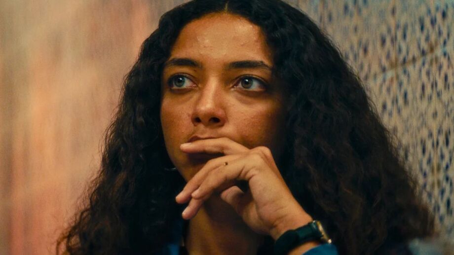 Na imagem, Fátima, personagem interpretado por Alice Carvalho no filme O Agente Secreto, está em destaque, com o fundo desforcado