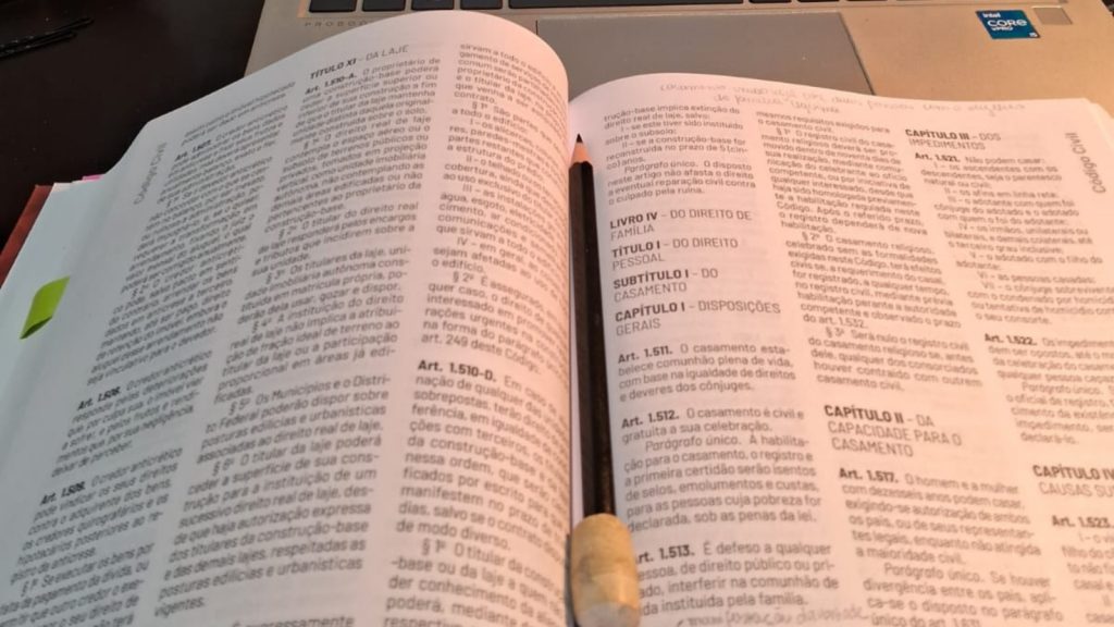 Imagem do livro jurídico aberto sobre uma mesa, visto de cima. Um lápis está apoiado entre as páginas abertas.