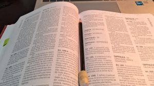 Imagem do livro jurídico aberto sobre uma mesa, visto de cima. Um lápis está apoiado entre as páginas abertas.