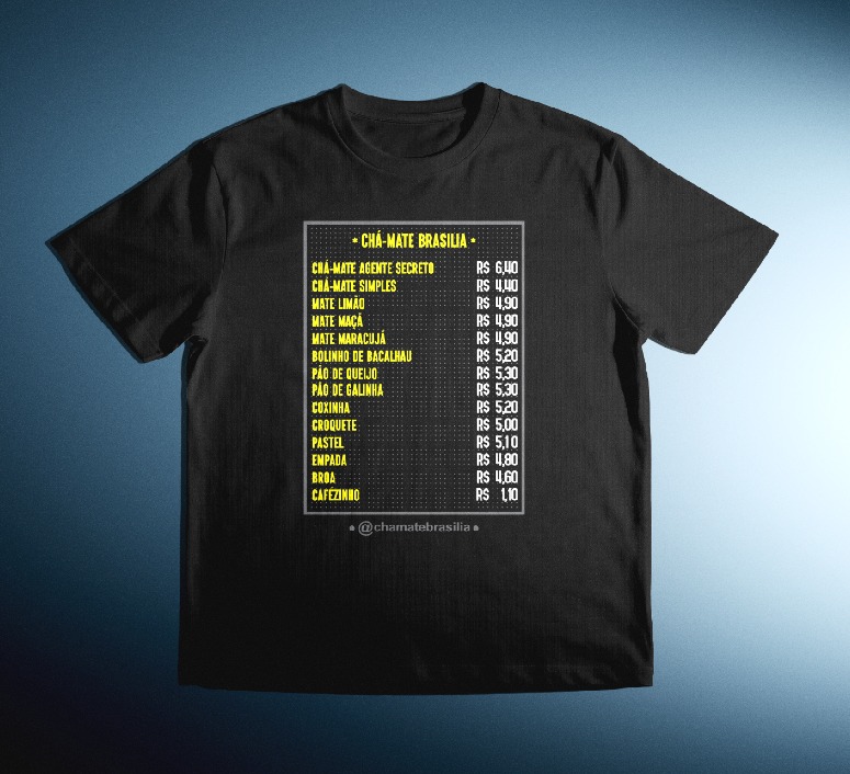 A imagem mostra uma camiseta preta com um design impresso na frente que imita um cardápio de lanchonete. O título do cardápio é “CHÁ-MATE BRASÍLIA”, escrito em letras grandes. Abaixo, há uma lista de bebidas e salgados típicos brasileiros, como chá-mate, coxinha, pastel e pão de queijo, acompanhados de seus respectivos preços em reais. As letras são amarelas e brancas, lembrando os letreiros de barracas de rua. O estilo é informal e cultural, celebrando a culinária popular brasileira de forma criativa e divertida.