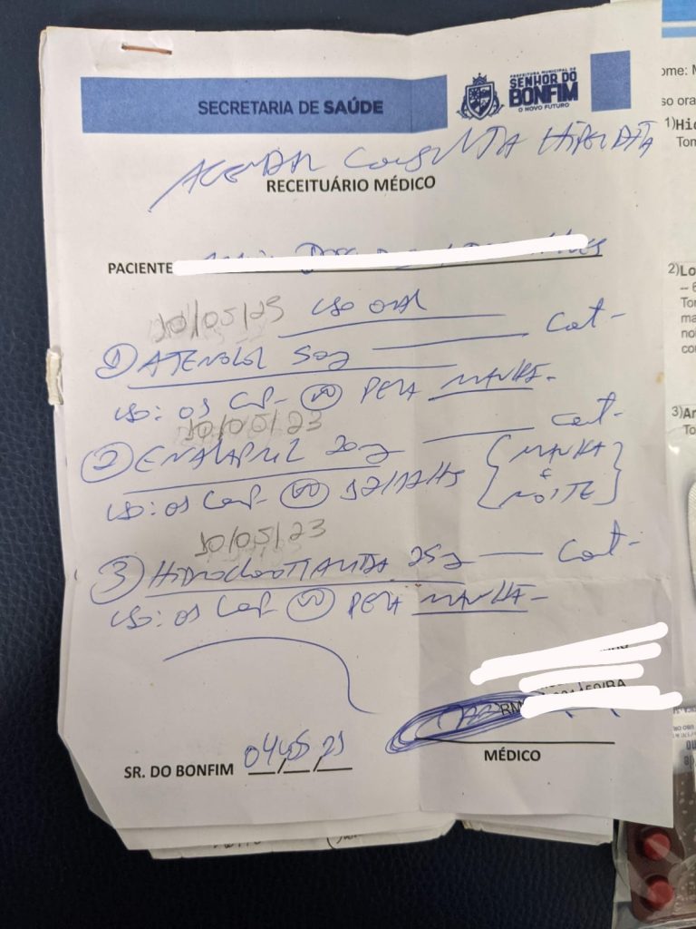 A foto mostra uma folha de receituário médico oficial, com o cabeçalho da Secretaria de Saúde de Senhor do Bonfim. O documento tem anotações manuscritas em letra cursiva, listando medicamentos, dosagens e horários de uso. Algumas informações pessoais estão cobertas para preservar a privacidade. No final da página, há assinatura e data do médico. Em resumo, é uma receita médica simples e manuscrita, usada para orientar o paciente sobre quais remédios tomar e em que momentos do dia.