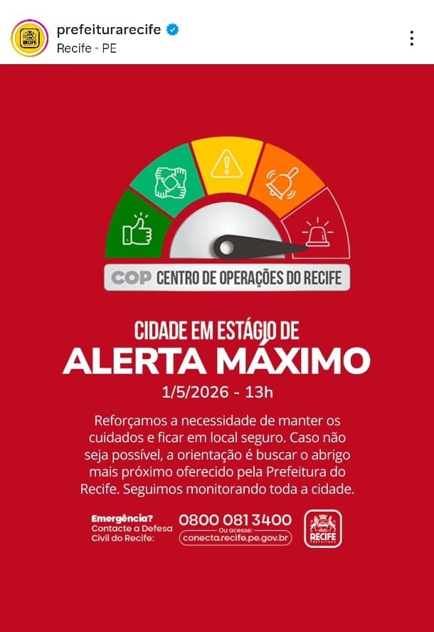 A imagem mostra um aviso oficial da Prefeitura do Recife. O fundo é vermelho e há um medidor com faixas coloridas (verde, amarelo, laranja e vermelho). O ponteiro está na faixa vermelha, indicando “Alerta Máximo”. O texto informa que, em 1º de maio de 2026 às 13h, a cidade está em nível máximo de alerta, orientando moradores a se manterem seguros e buscarem abrigo se necessário. Também aparecem os contatos de emergência: telefone 0800 081 3400 e o site conecta.recife.pe.gov.br