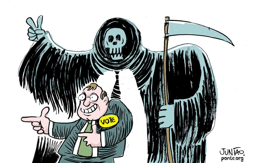 A charge mostra um político sorridente pedindo votos, enquanto uma figura da morte, empunhando uma foice, aparece atrás dele, sugerindo uma relação entre política e crime ou violência.