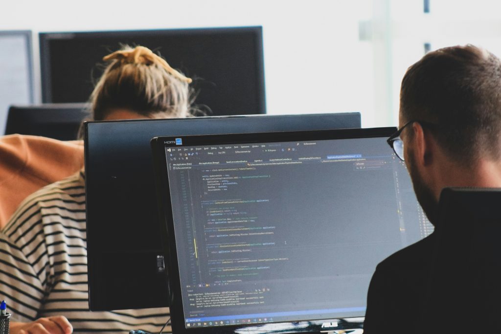 Duas pessoas trabalhando em código de computador em monitores em um espaço de trabalho iluminado