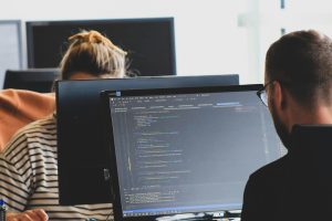 Duas pessoas trabalhando em código de computador em monitores em um espaço de trabalho iluminado